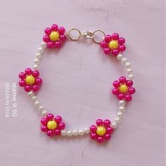 a pink and yellow beaded bracelet with flowers on it's end, sitting on a table