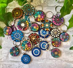 a bunch of colorful key chains sitting on top of a white brick wall next to green leaves