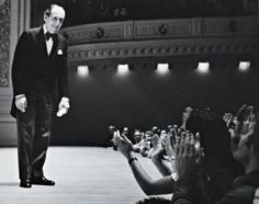 a man in a tuxedo is standing on the stage with his hands up