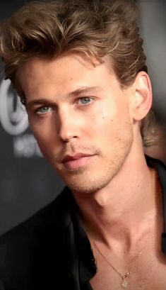 a close up of a person wearing a black shirt and necklace with blue eyes in front of a dark background