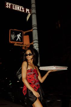 a woman standing on the street holding a pizza box in her hand and wearing sunglasses