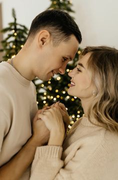 a man and woman standing in front of a christmas tree with their hands on each other's chest