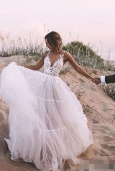 a woman in a white dress is walking on the sand