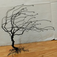 a wire tree sculpture sitting on top of a wooden floor next to a white wall