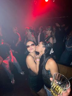 two women kissing each other in front of a crowd at a club or bar with red lights