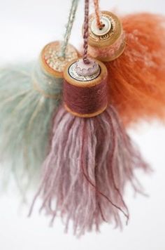 two spools of thread are hanging from twine with beads and feathers on them