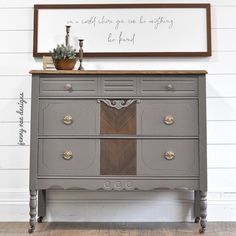 an old dresser is painted gray with gold hardware and wood accents, along with a framed sign