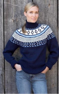 a woman standing in front of a wooden fence wearing a blue sweater with white and black designs on it