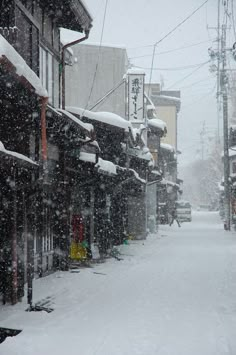 a snow covered street with buildings and power lines in the background, during a winter storm