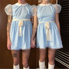 two women in blue dresses standing next to each other with tattoos on their arms and legs