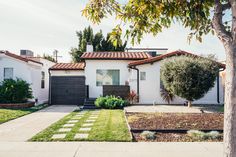 a white house with a tree in front of it and grass on the side yard