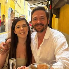 a man sitting next to a woman at a table in front of a yellow building