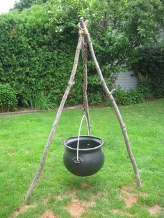 a black pot hanging from a wooden pole in the grass with two sticks sticking out of it