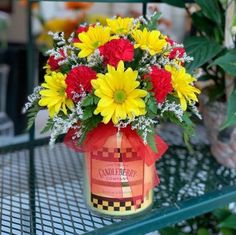 a vase filled with yellow and red flowers sitting on top of a green metal table