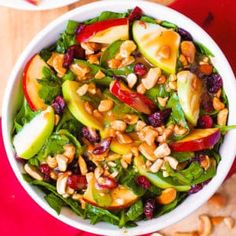 a salad with apples, cranberries and nuts in a white bowl on a red surface