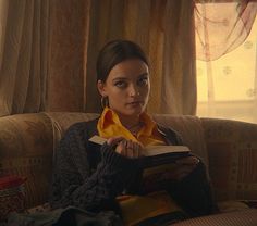 a woman sitting on a couch holding a book in her hands and looking at the camera