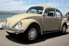 an old vw bug is parked on the side of the road by the water