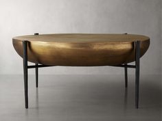 an oval coffee table with black legs and gold leaf design on the top, against a gray background