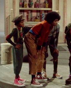 three young boys standing on the sidewalk in front of a store window with their hands together