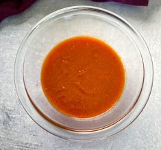 a glass bowl filled with red sauce on top of a white tablecloth next to a purple towel