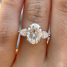 a woman's hand holding a three stone engagement ring with two diamonds on it