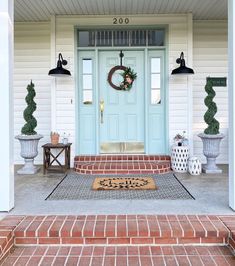 a blue front door with two wreaths on the steps and potted plants next to it