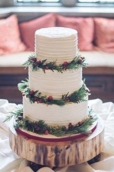 a three tiered white wedding cake with pine branches and berries