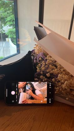 someone taking a photo of flowers with their cell phone on the table next to them