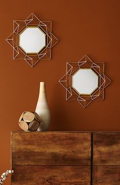 two mirrors are hanging on the wall above a dresser with a vase and other items