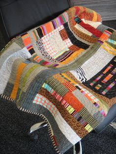 a chair with a quilt on it in front of a black wall and carpeted floor