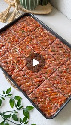 a pan filled with meat sitting on top of a table next to green plants and potted