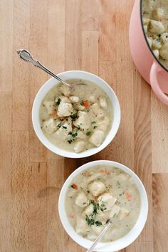 two bowls of chicken and dumpling soup on a wooden table next to a pink pot