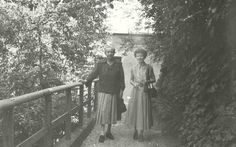 an old black and white photo of two people standing next to each other on a bridge