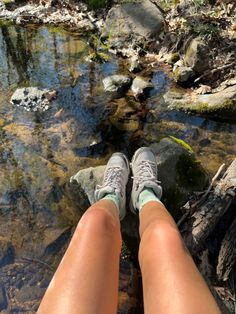 the legs of a person who is sitting on rocks near a stream with clear water