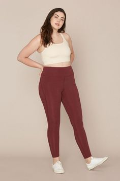 a woman standing with her hands on her hips wearing maroon pants and a white tank top