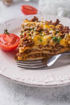 a slice of lasagna on a white plate with a fork and cherry tomatoes