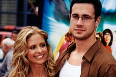 a man and woman standing next to each other in front of a movie poster on the wall