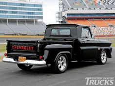 an old black pickup truck parked in front of a football stadium with the word chevrolet on it