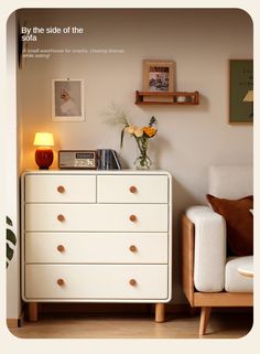 a white dresser sitting in a living room next to a chair and wall with pictures on it