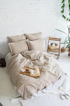 an unmade bed with two pillows and some food on it in front of a white brick wall