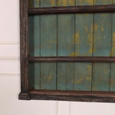 an old wooden shelf with green paint on the top and bottom, hanging from a white wall