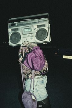 a woman carrying an old fashioned boombox on her head with a purple bag over her shoulder