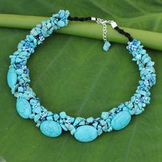 a necklace with turquoise stones and beads on a green leaf