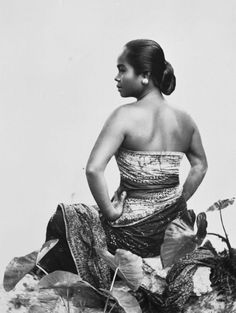 an old photo of a woman sitting on top of a leafy plant with her hands in her pockets