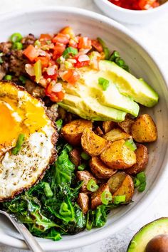 a white bowl filled with vegetables and an egg on top of some sort of meat