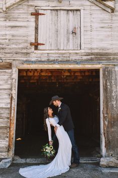 a bride and groom kissing in front of an old wooden barn with the doors open