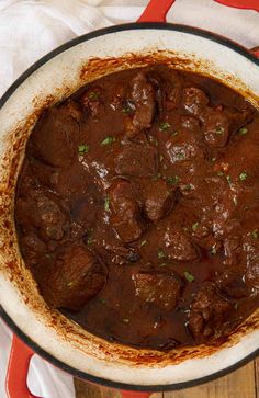 a pot filled with meat and sauce on top of a wooden table next to a white towel