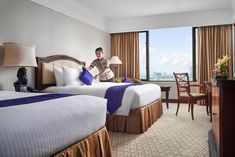 a man in a hotel room with two beds and a large window overlooking the ocean