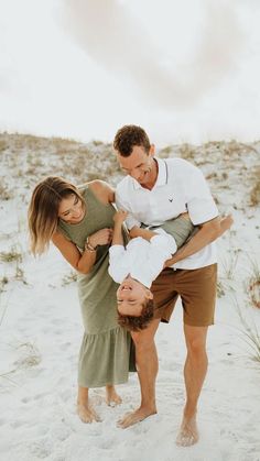 three people standing in the sand with their arms around each other and one person laying on his back