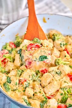 a wooden spoon scooping food out of a pan with broccoli and tomatoes